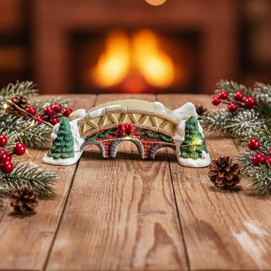 Decorative Christmas bridge with trees and berries on a wooden table in front of a fireplace.