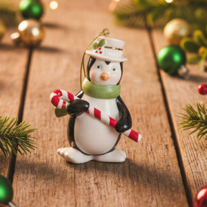 Penguin ornament holding a candy cane on a wooden surface with Christmas decorations.