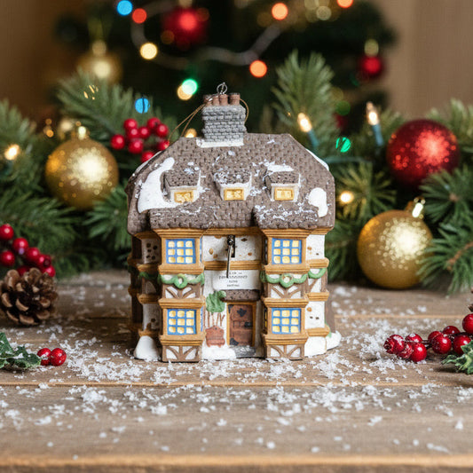 Decorative Christmas house on a table with a festive background featuring a tree and ornaments.