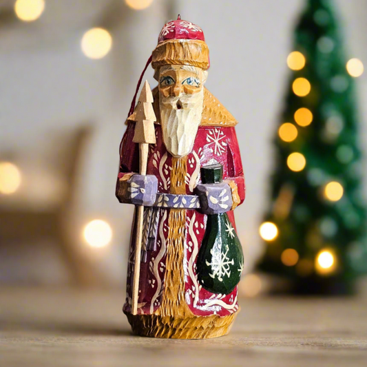 Decorative figure of a bearded man with a red hat and coat, standing in front of a blurred Christmas tree and lights.
