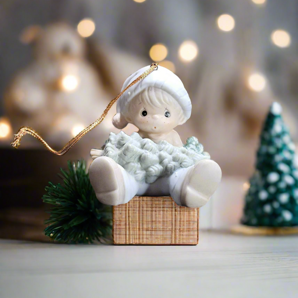 Decorative figurine of a child with a sheep in a basket, surrounded by festive lights and trees.